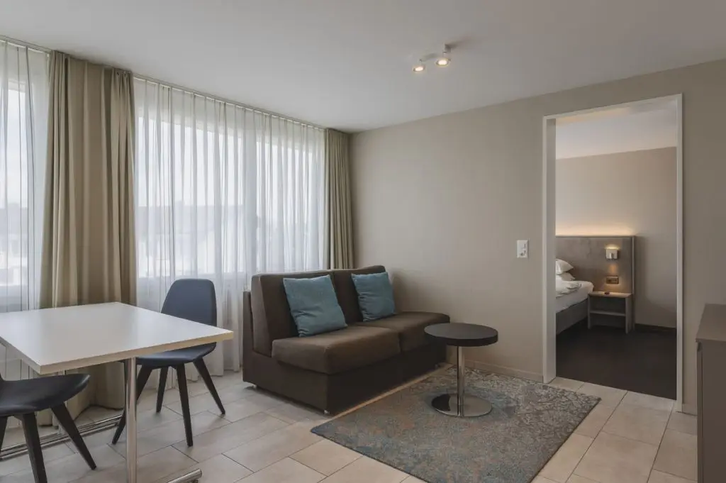 Serviced Apartments Zurich Airport Kitchen and Living Room with dining table, sofa, coffee table and TV.
